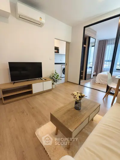 Modern living room with wooden flooring, TV, and cozy decor leading to a bedroom with a view.