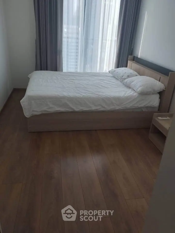 Modern bedroom with wooden flooring and large window for natural light.