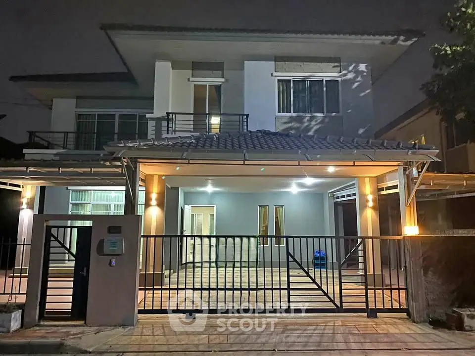 Modern two-story house with gated entrance and exterior lighting at night.