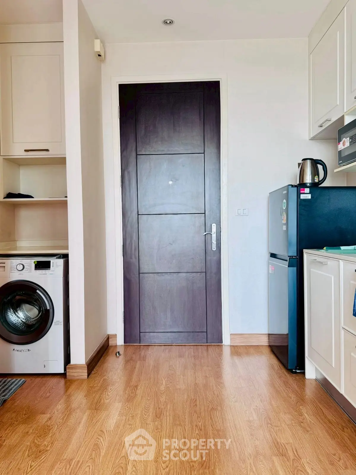 Modern kitchen with wooden flooring, washing machine, and sleek appliances in a cozy apartment.