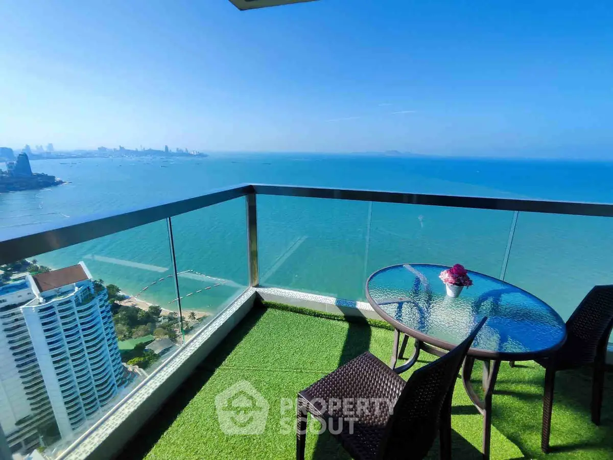 Stunning ocean view from a high-rise balcony with glass railing and outdoor seating.