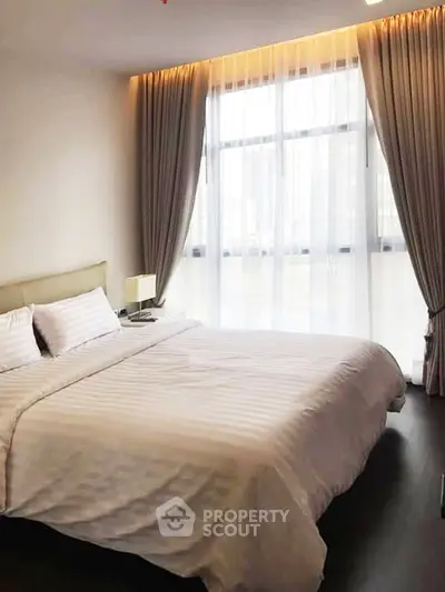 Spacious bedroom with large window and elegant curtains in modern apartment.