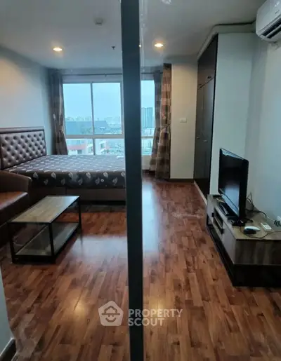 Modern studio apartment with wooden flooring and city view, featuring a cozy bed and entertainment area.