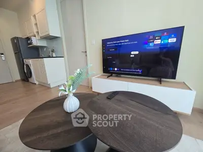 Modern living room with smart TV, stylish coffee tables, and compact kitchen area.