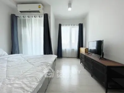 Modern bedroom with natural light, featuring a bed, TV, and air conditioning.