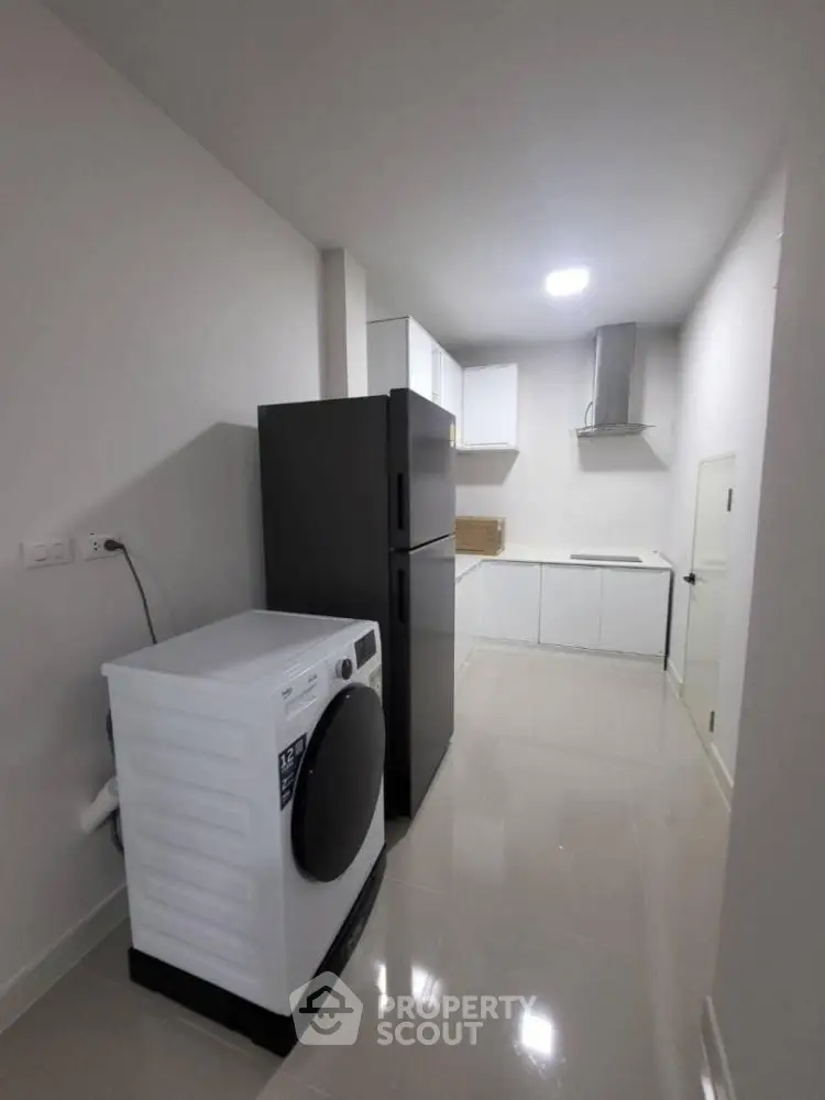 Modern kitchen with sleek appliances and glossy flooring, featuring a washing machine and refrigerator.