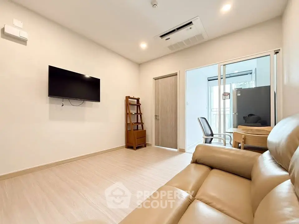 Modern living room with beige leather sofa and wall-mounted TV in a cozy apartment.