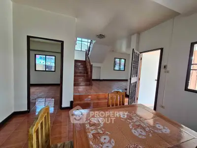 Spacious interior with wooden furniture and tiled flooring, featuring a staircase and multiple windows.