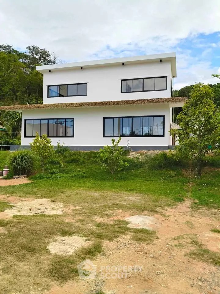 Modern two-story house with large windows and lush greenery