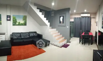 Modern living room with stylish staircase and dining area, featuring sleek black furniture and vibrant decor.