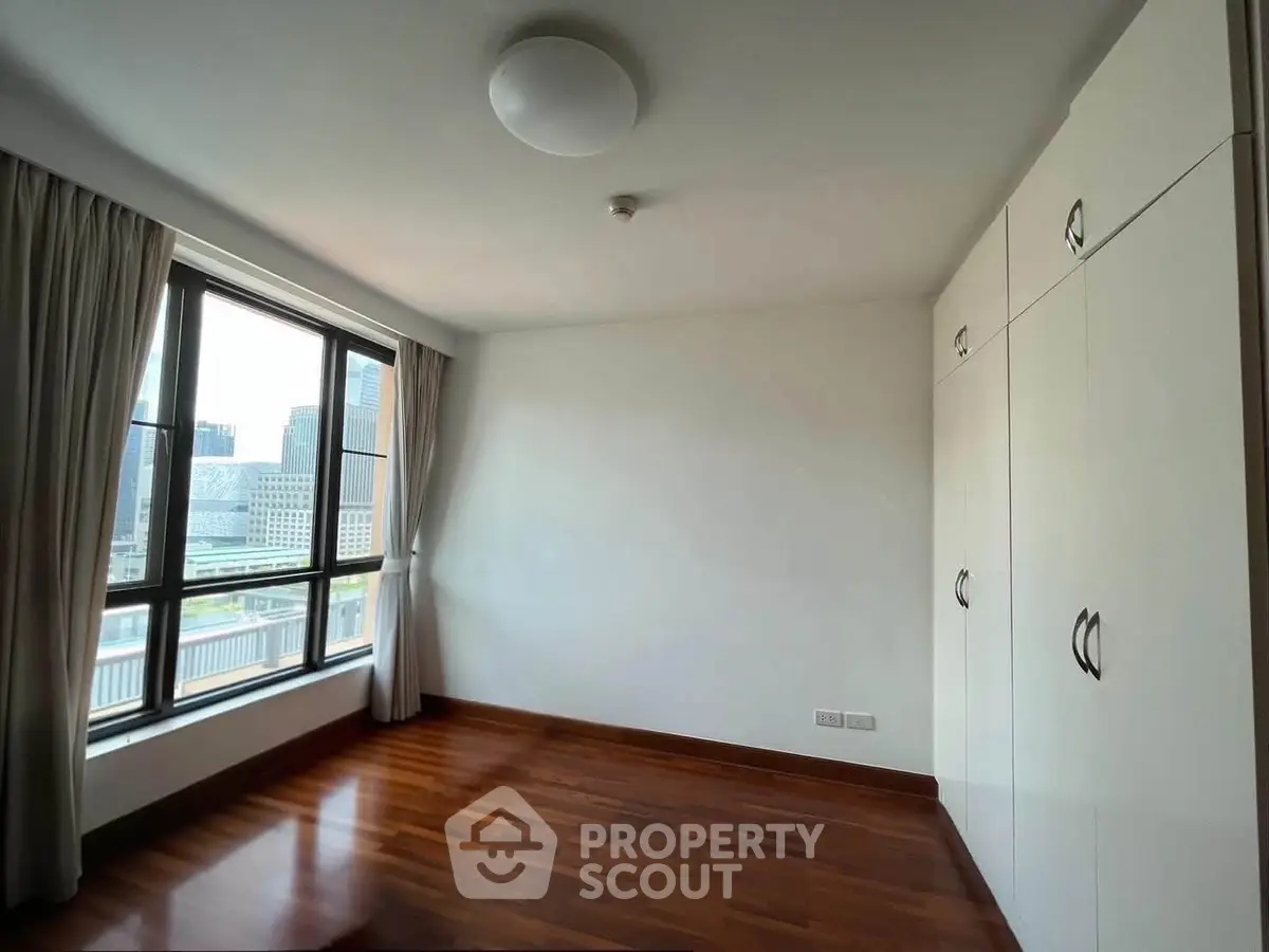 Spacious bedroom with city view and built-in wardrobe, featuring elegant wooden flooring and large windows.