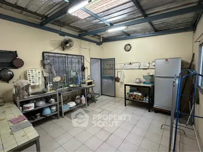 Spacious kitchen with tiled floor, metal shelving, and large refrigerator in a cozy home setting.