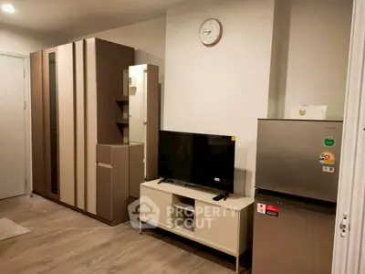 Modern living room with sleek furniture and appliances, featuring a TV and refrigerator.