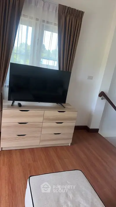 Cozy living room with modern TV setup and wooden flooring, perfect for relaxation.