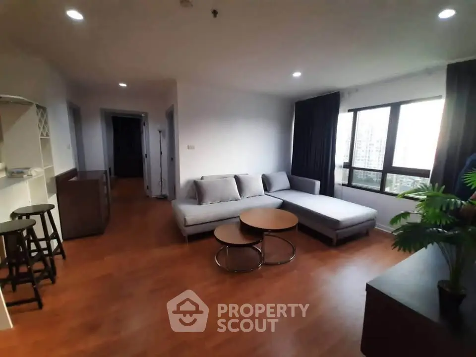 Spacious living room with modern furniture and large window offering city views.