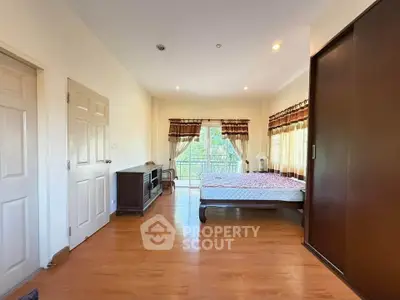 Spacious bedroom with wooden flooring and large windows opening to a balcony, offering ample natural light.