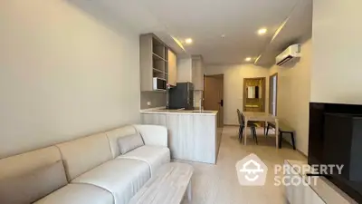 Modern living room with open kitchen and dining area, featuring sleek furniture and neutral tones.