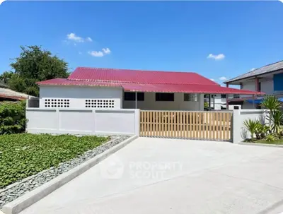 Charming single-story home with red roof and spacious driveway under clear blue sky.