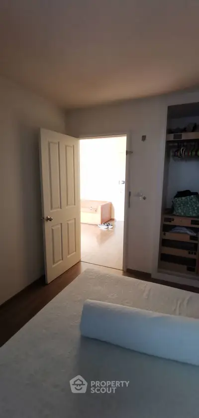 Cozy bedroom with open door leading to a bright living area, featuring a neatly organized closet.