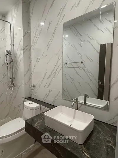 Modern bathroom with marble walls and sleek fixtures, featuring a stylish vanity and mirror.