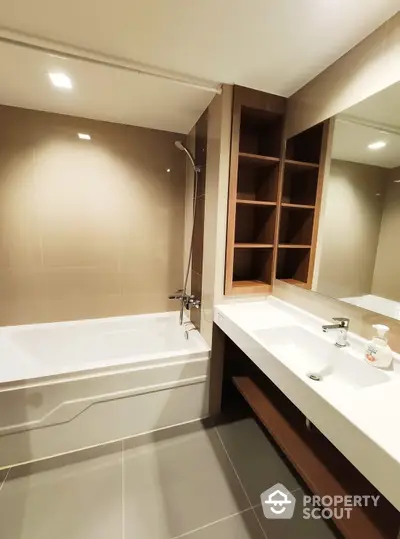 Spacious modern bathroom with a large tub, sleek fixtures, ample lighting, and built-in wooden shelving, perfect for a relaxing retreat.