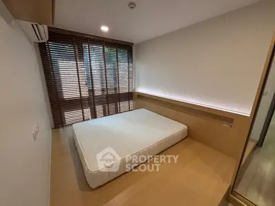 Modern minimalist bedroom with wooden flooring and large window blinds.