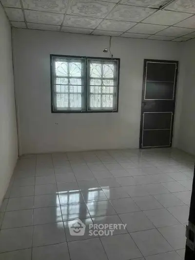 Spacious empty room with tiled flooring and window, ready for customization.