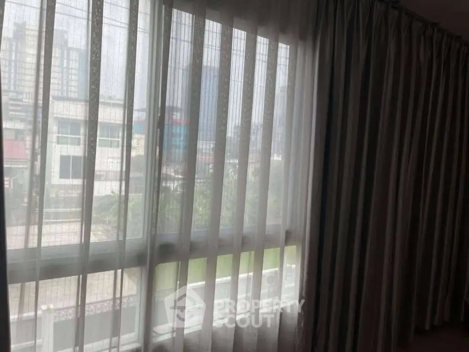 Spacious room with large window and sheer curtains offering a city view.