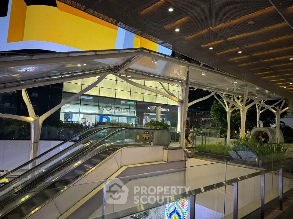 Modern shopping mall entrance with escalators and illuminated signage at night.