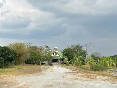 Charming countryside house with lush greenery and expansive driveway under a cloudy sky.