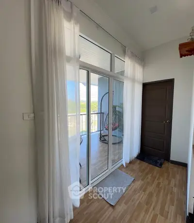 Bright balcony with glass doors and sheer curtains, offering a serene outdoor view.