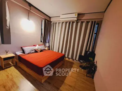 Cozy bedroom with red bedding and wooden flooring, featuring air conditioning and natural light.