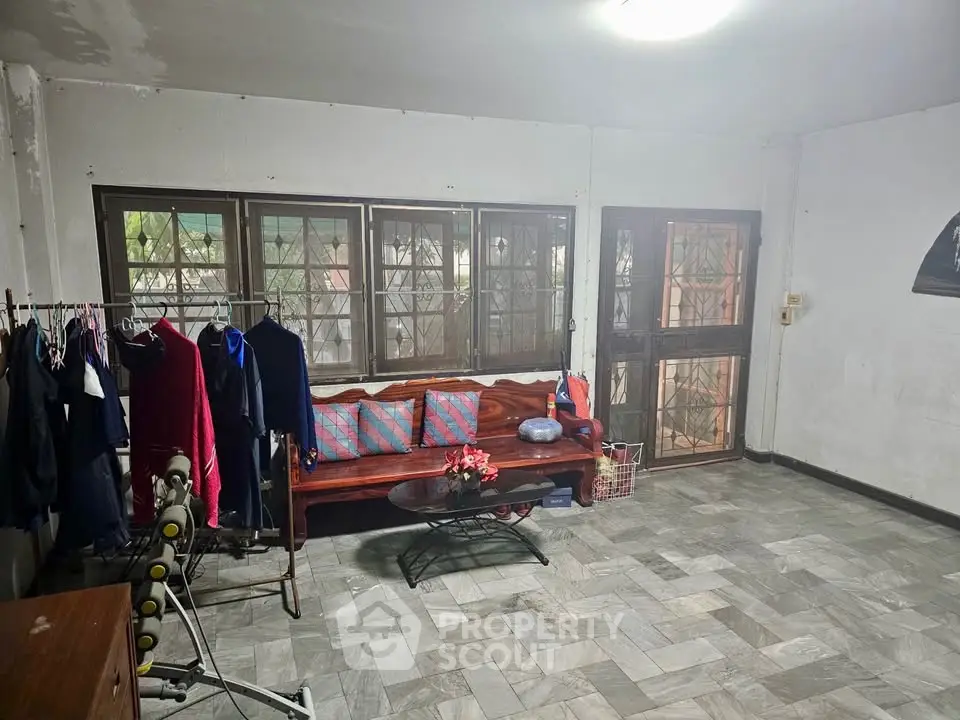 Spacious living room with large windows and tiled flooring, featuring a cozy seating area and ample natural light.