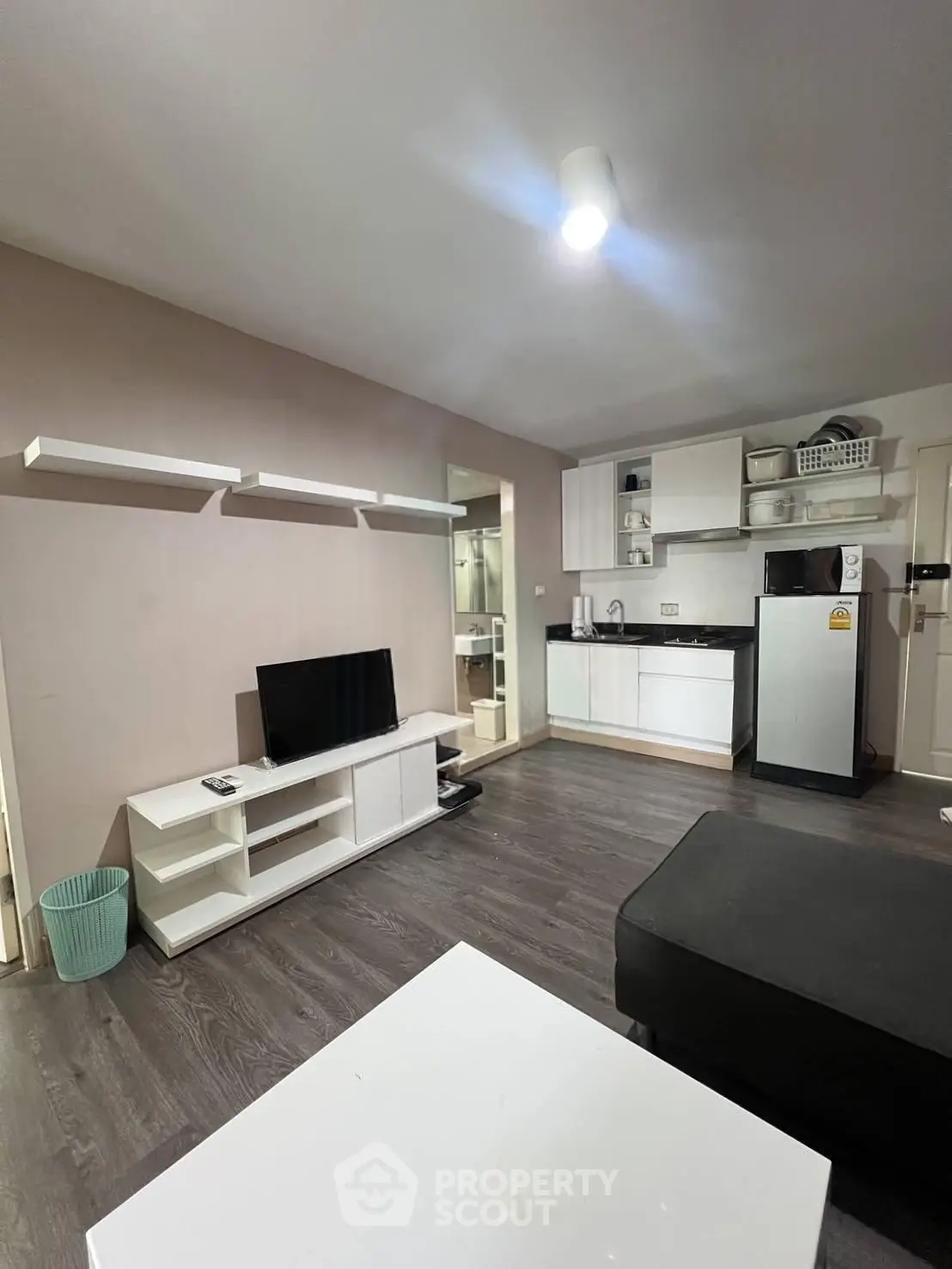 Modern living room with sleek kitchen, TV unit, and stylish shelving in a cozy apartment.