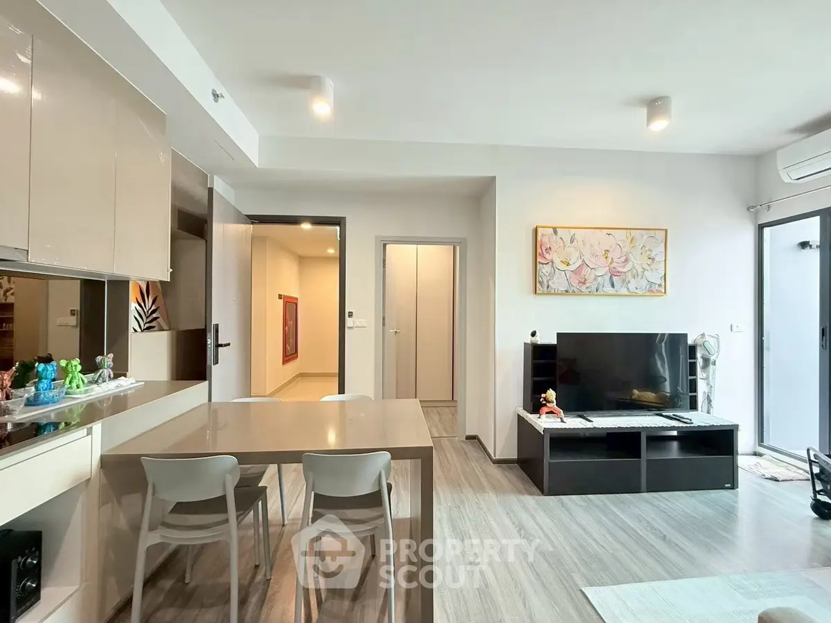 Modern living room with sleek furniture and open layout, featuring a stylish dining area and large TV setup.