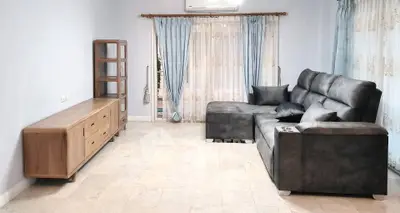 Spacious living room with modern gray sofa and elegant wooden furniture, featuring large windows with blue curtains.