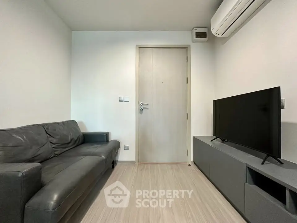 Modern living room with sleek black sofa and flat-screen TV, featuring minimalist design and air conditioning.