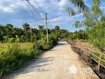 Serene country road flanked by lush greenery and traditional fencing, leading to a tranquil rural landscape perfect for a peaceful living experience.