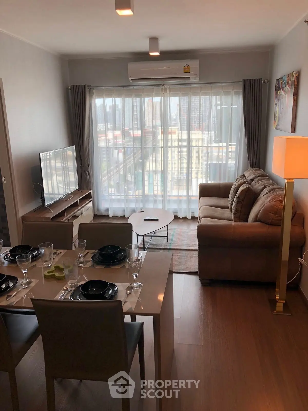 Modern living room with city view, cozy sofa, dining area, and large windows.