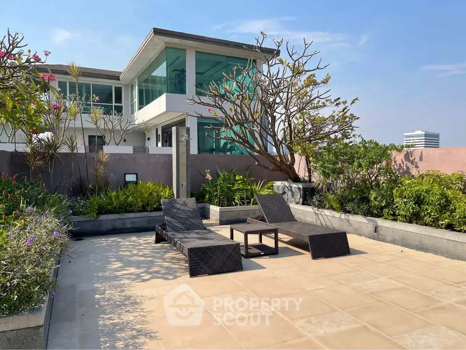 Luxurious rooftop terrace with modern lounge chairs and lush greenery, offering a serene escape with city views.