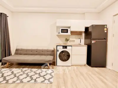 Modern studio apartment with sleek kitchenette and cozy living area, featuring a washing machine and fridge.