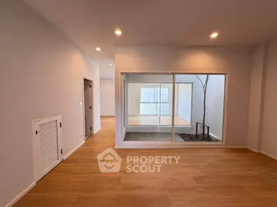 Spacious modern living area with wooden flooring and large glass doors leading to a bright courtyard.