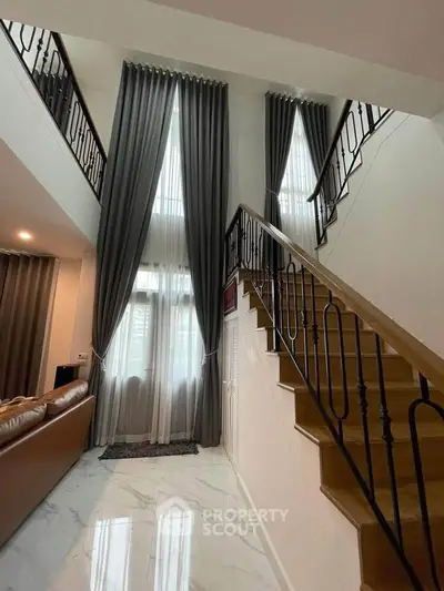 Elegant duplex interior with high ceilings and stylish staircase, featuring luxurious curtains and modern design.