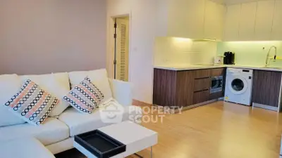 Modern living room with open kitchen, featuring stylish sofa and washing machine.