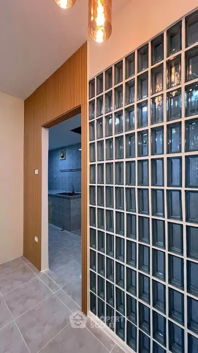 Modern interior with glass block wall and wooden accents leading to a sleek kitchen.