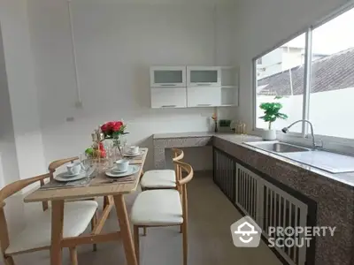 Modern kitchen with sleek countertops and dining area, featuring natural light and contemporary design.