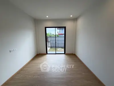 Spacious empty room with wooden flooring and large window overlooking garden
