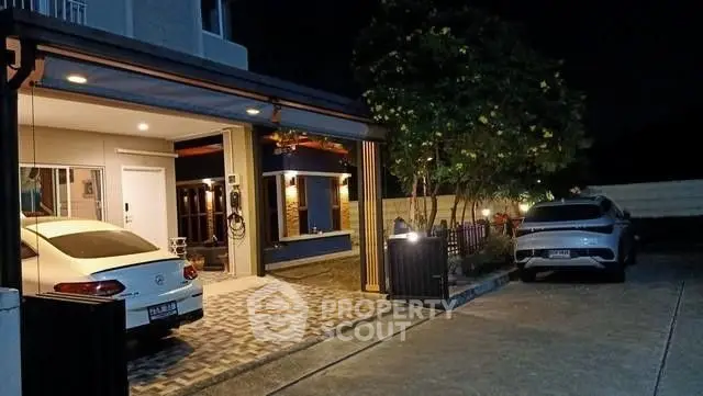 Modern home with spacious driveway and two cars parked at night, featuring sleek architecture.