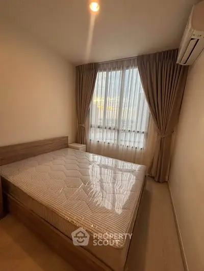 Cozy bedroom with natural light, featuring a large window, elegant curtains, and a comfortable bed.