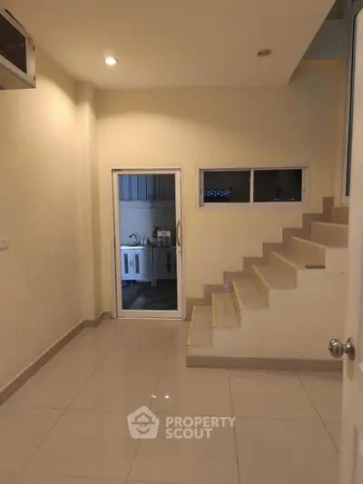 Modern interior with sleek staircase and tiled floor, featuring a compact kitchen area.